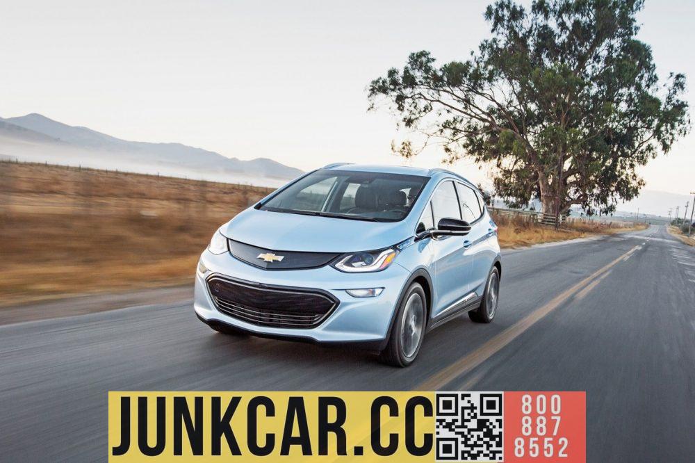 A 2017 Chevrolet Bolt EV drives down a country road with mountains and fields in the background.